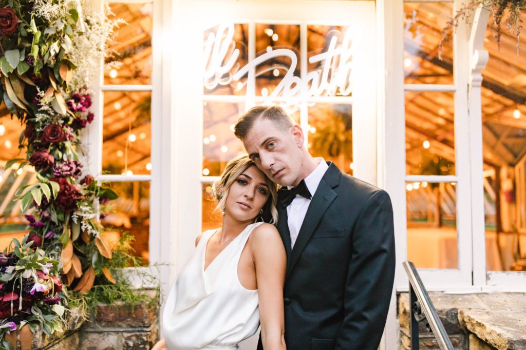 bride and groom pose in front of neon sign