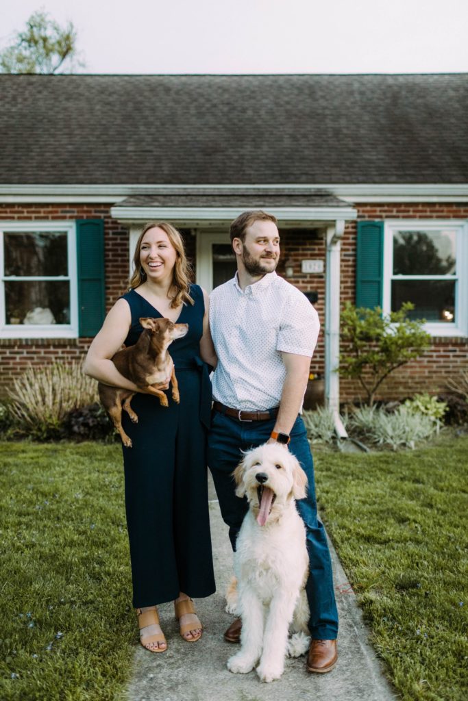 couple poses in front of their house with dog