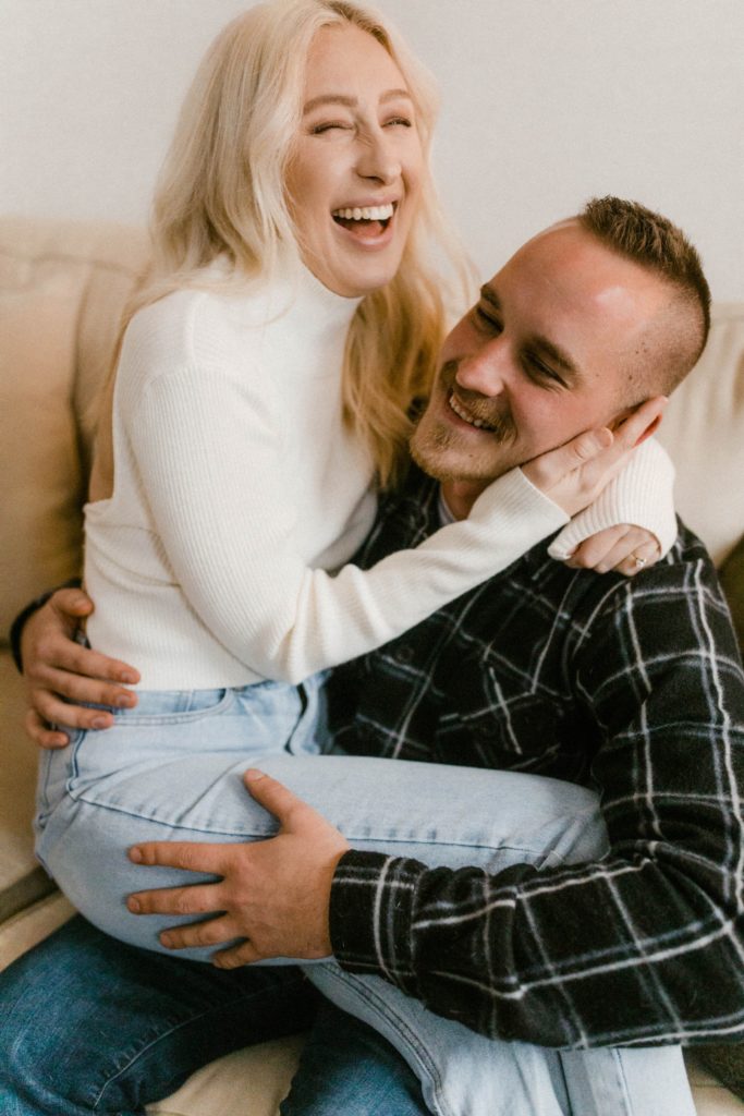 a couple laughing and snuggling on couch for in home engagement session