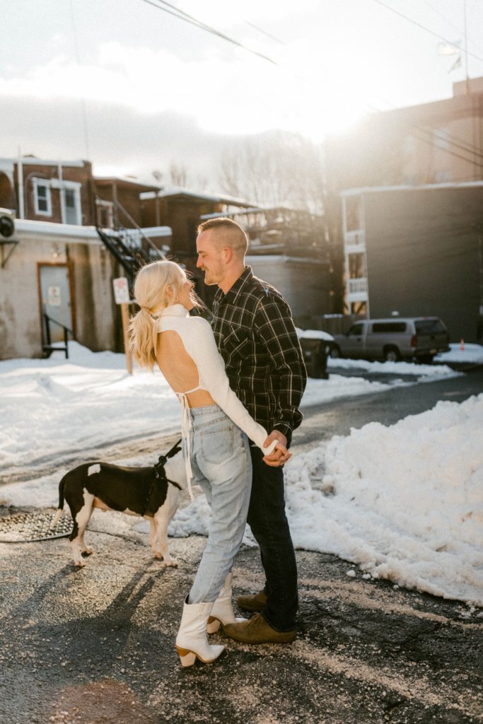 a couple snuggle and pose on snow covered street for winter engagement session 