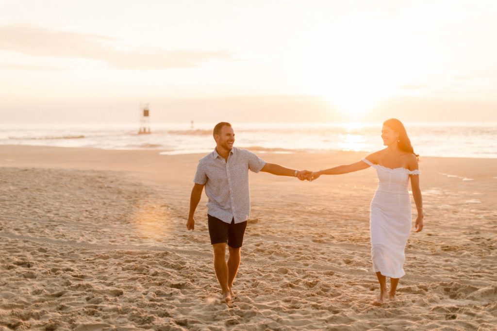 couple holding hands walking on beach at sunrise for sunrise rehoboth beach engagement session