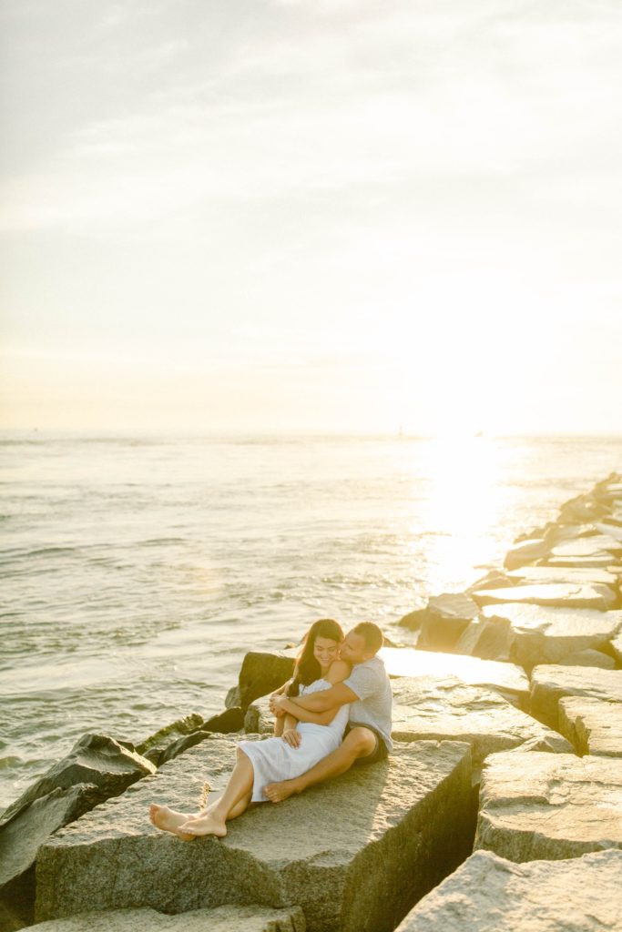 couple sitting on rocks at sunrise for sunrise rehoboth beach engagement session