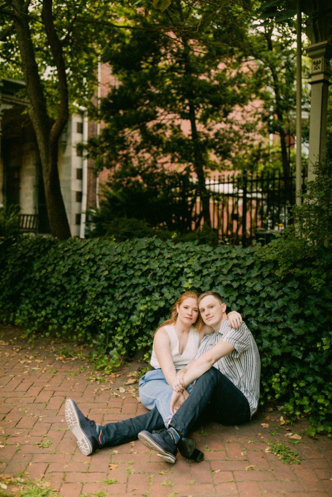 couple sitting on sidewalk posing in front of ivy 