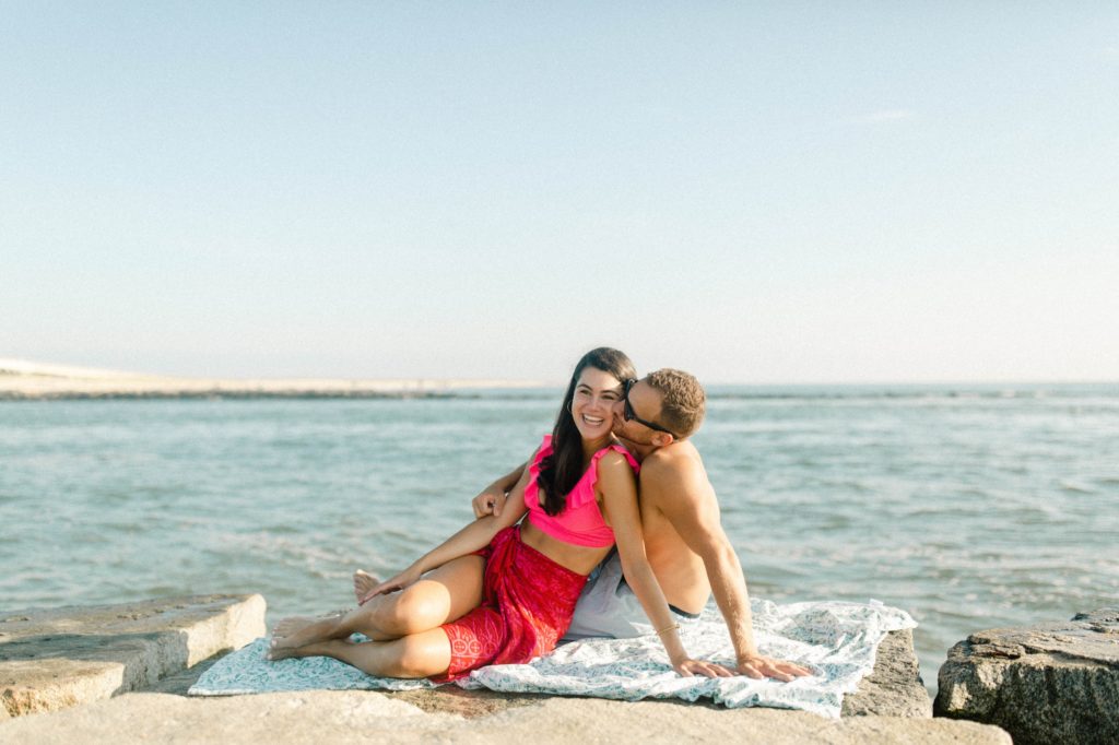 couple posing in bathing suits on rocks for sunrise rehoboth beach engagement session