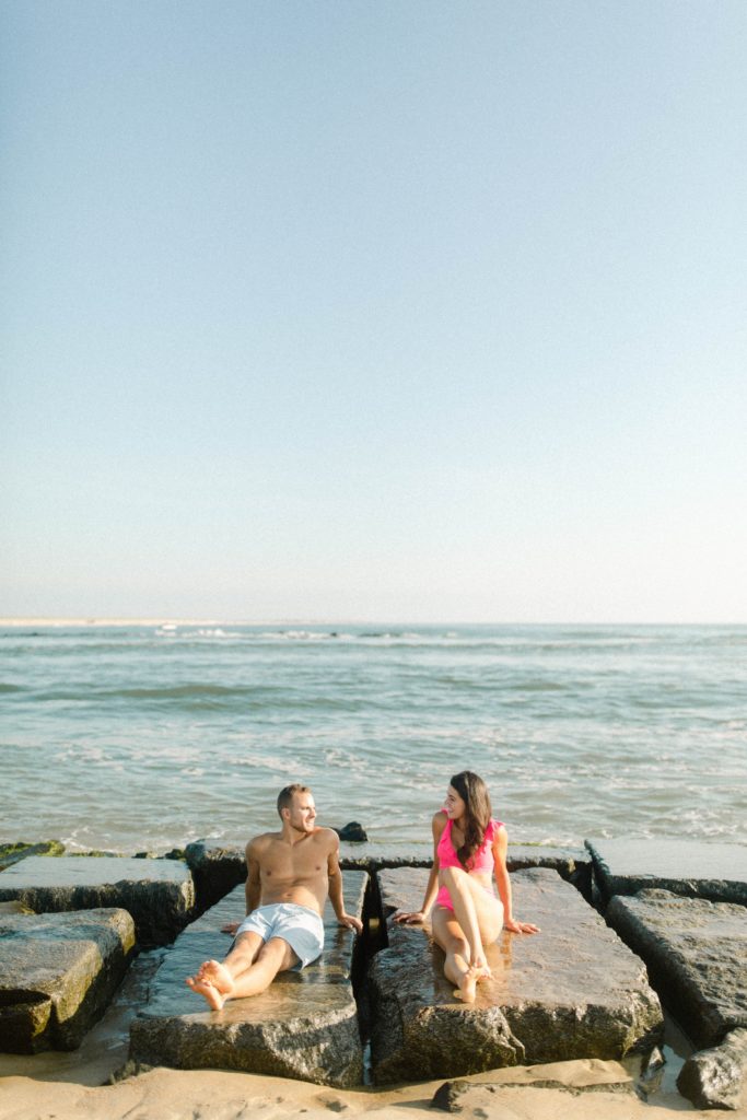 a couple sitting on rocks for sunrise rehoboth beach engagement session