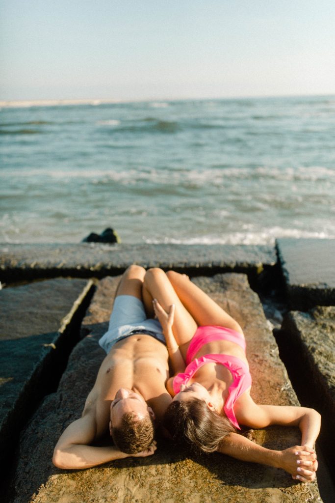 a couple laying on rocks in bathing suit for sunrise rehoboth beach engagement session