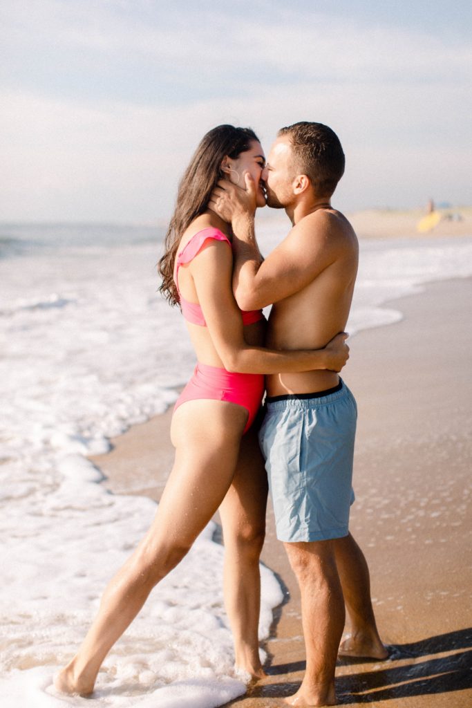 couple kiss on beach wearing bathing suits for sunrise rehoboth beach engagement session