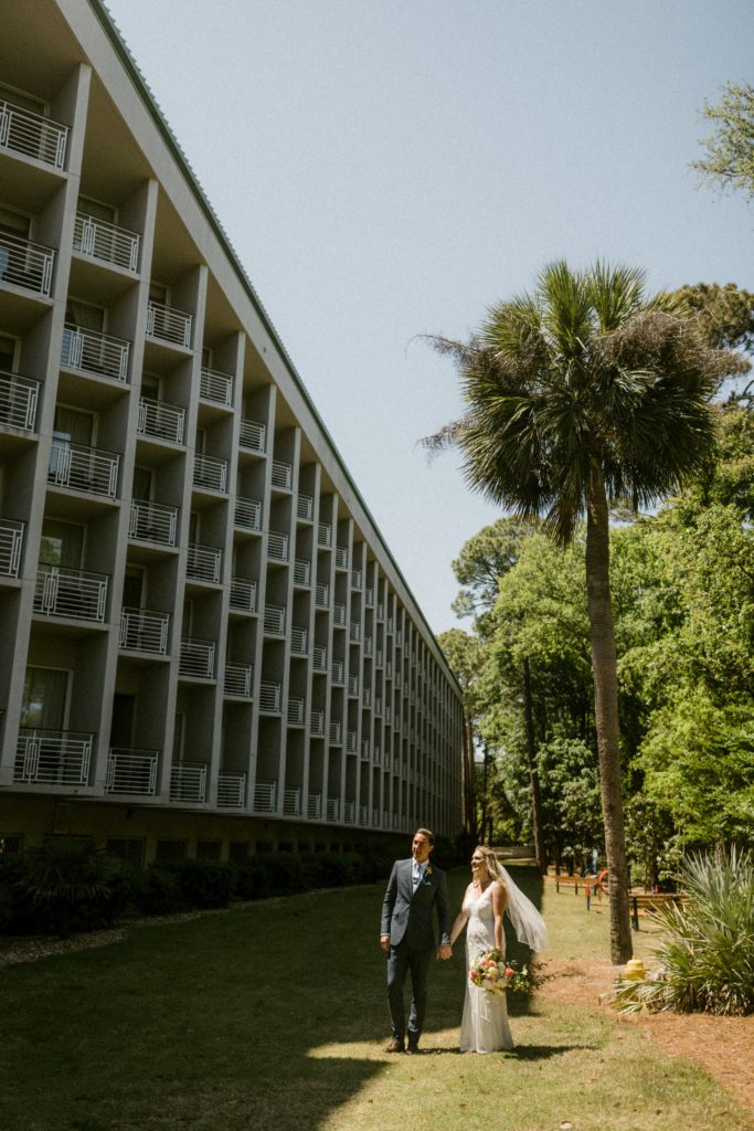 bride and groom pose in front of beach resort for hilton head beach wedding