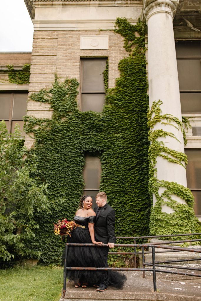 couple posing for anniversary session in front of ivy covered wall