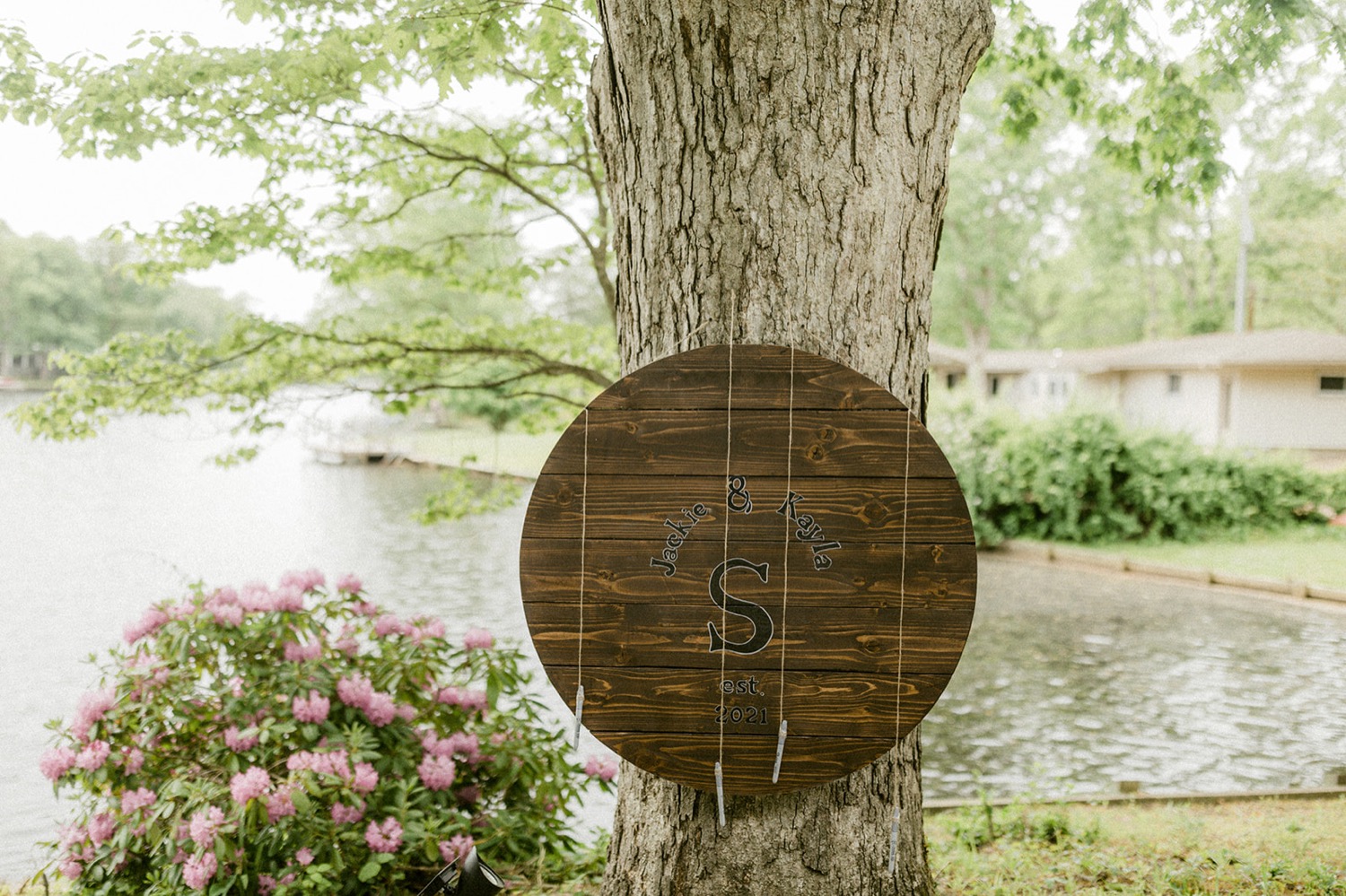 wooden guest book sign hanging on tree lakeside backyard micro wedding