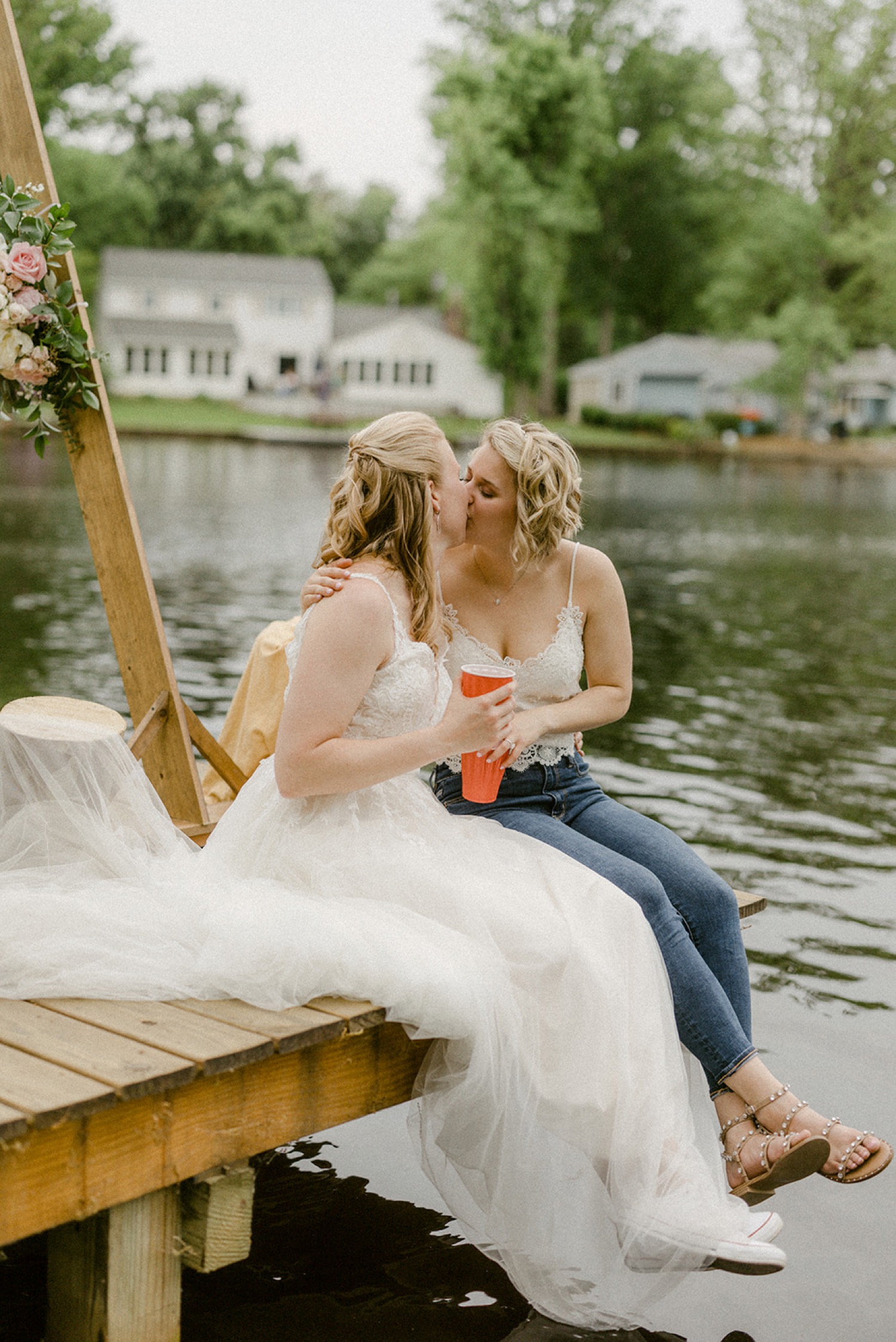 brides kissing on dock wearing jeans lakeside backyard micro wedding