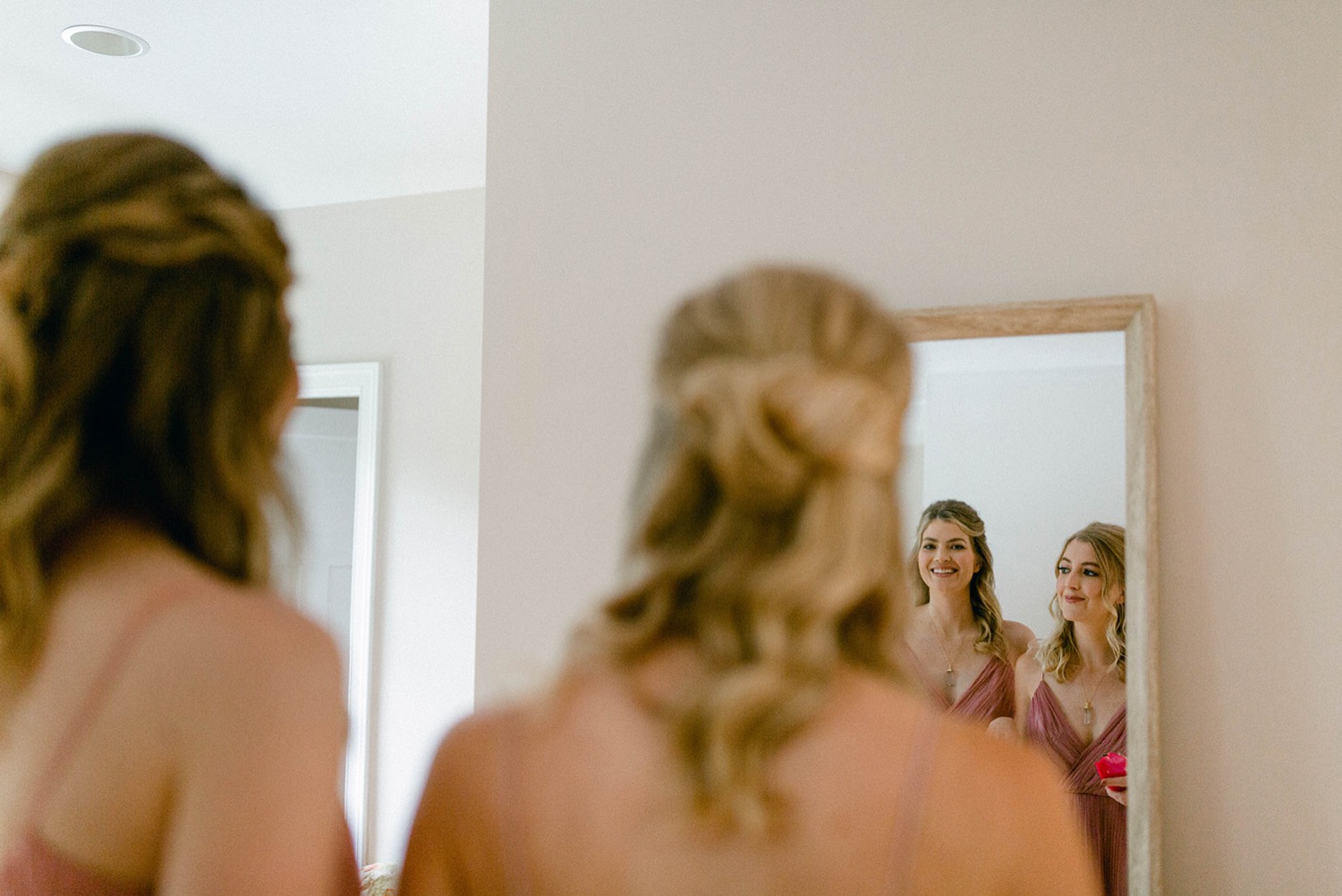 bridesmaids getting ready smiling into mirror reflection