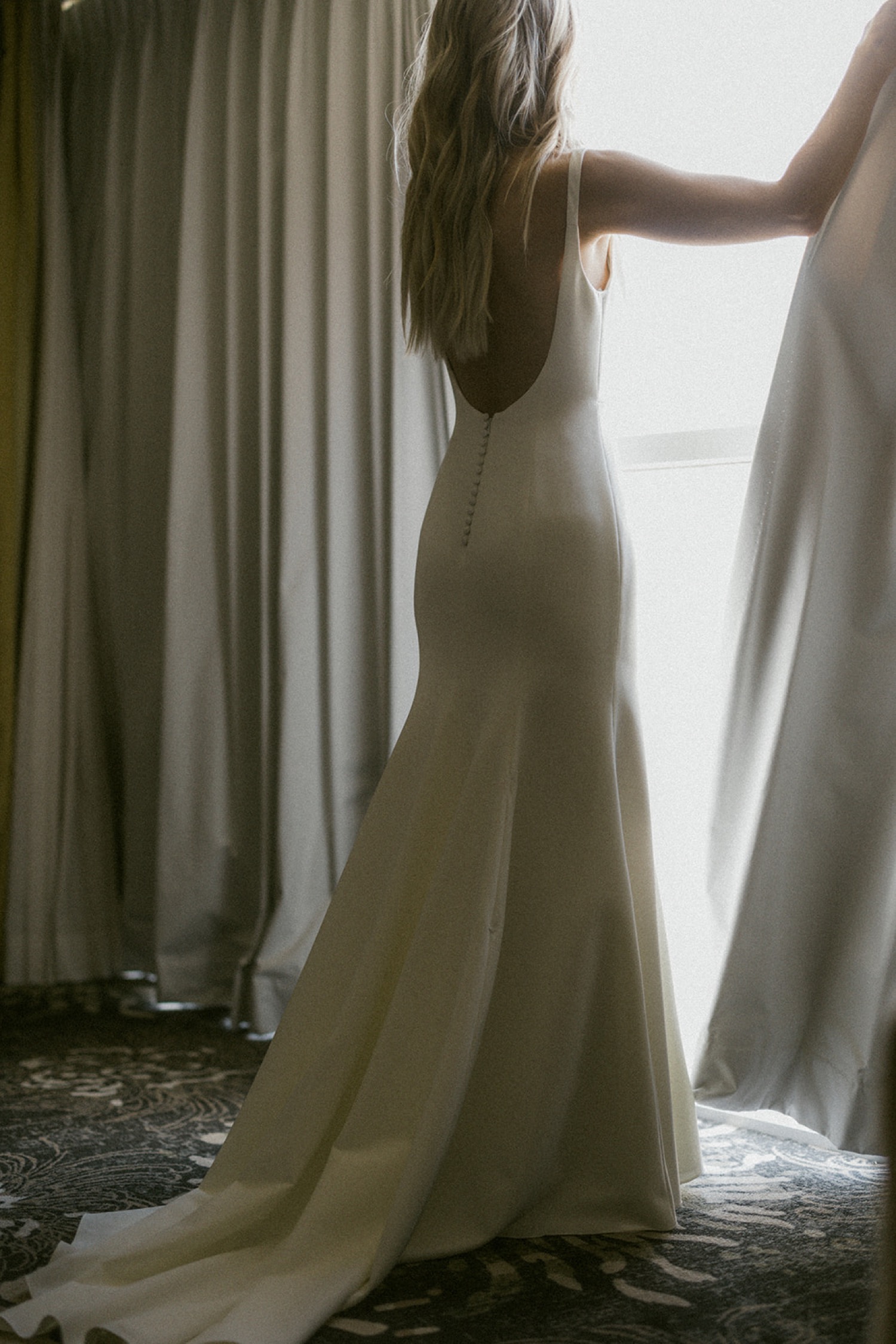 bride in wedding dress opening curtains