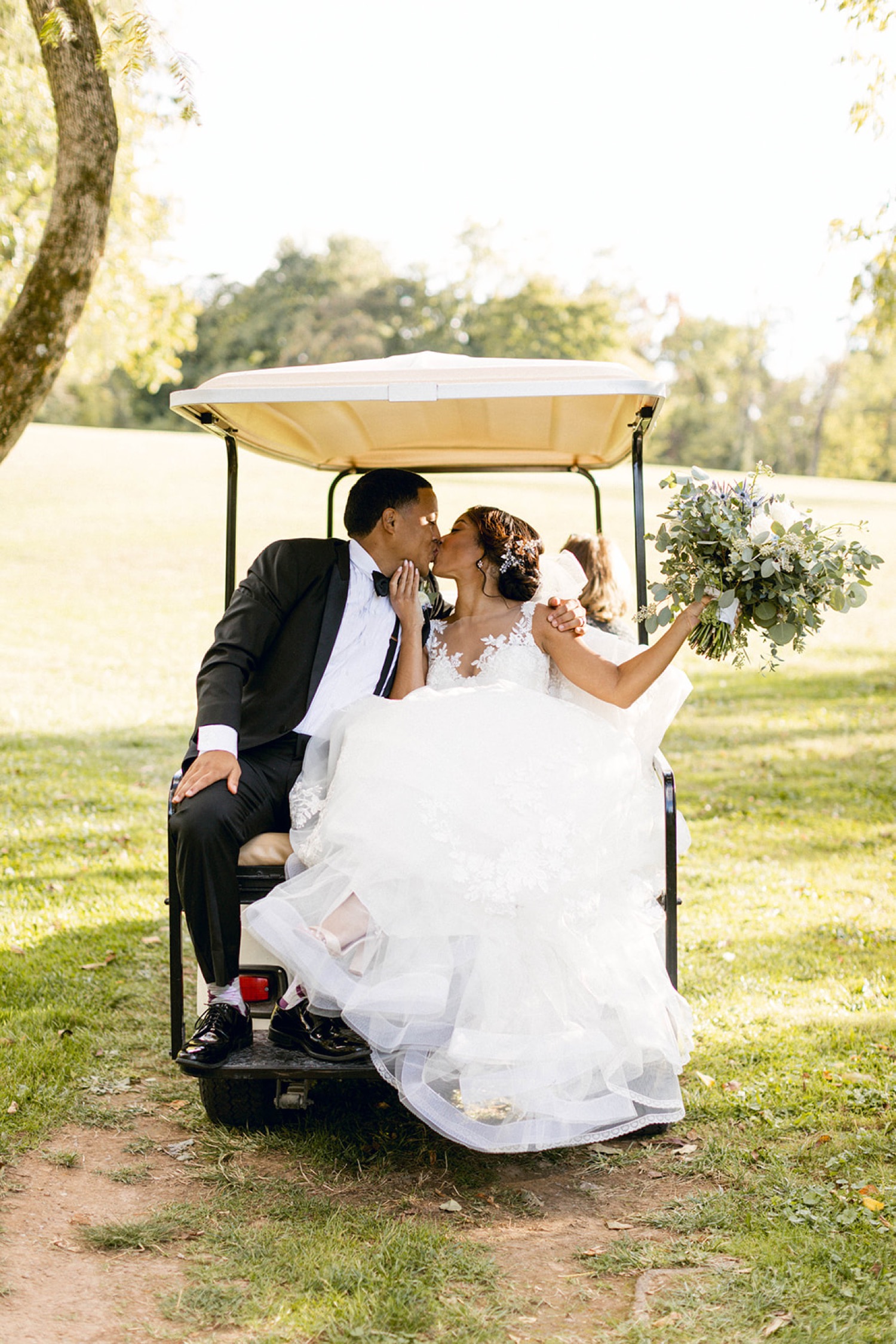 bride and groom in back of golf cart kissing