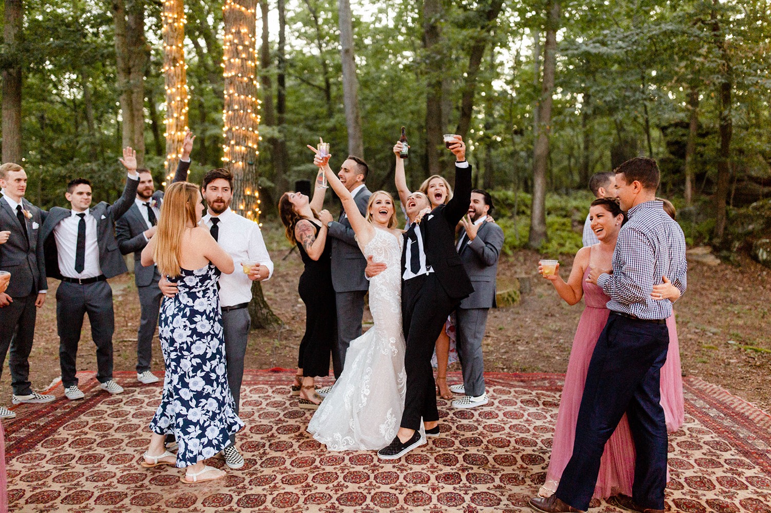 guests raising glasses celebrating dancing on carper in forest bohemian backyard wedding