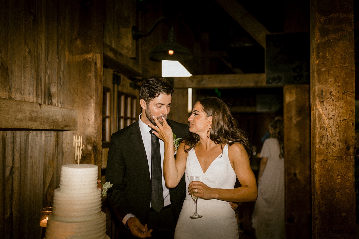 groom licking bride's finger white wedding cake rustic barn