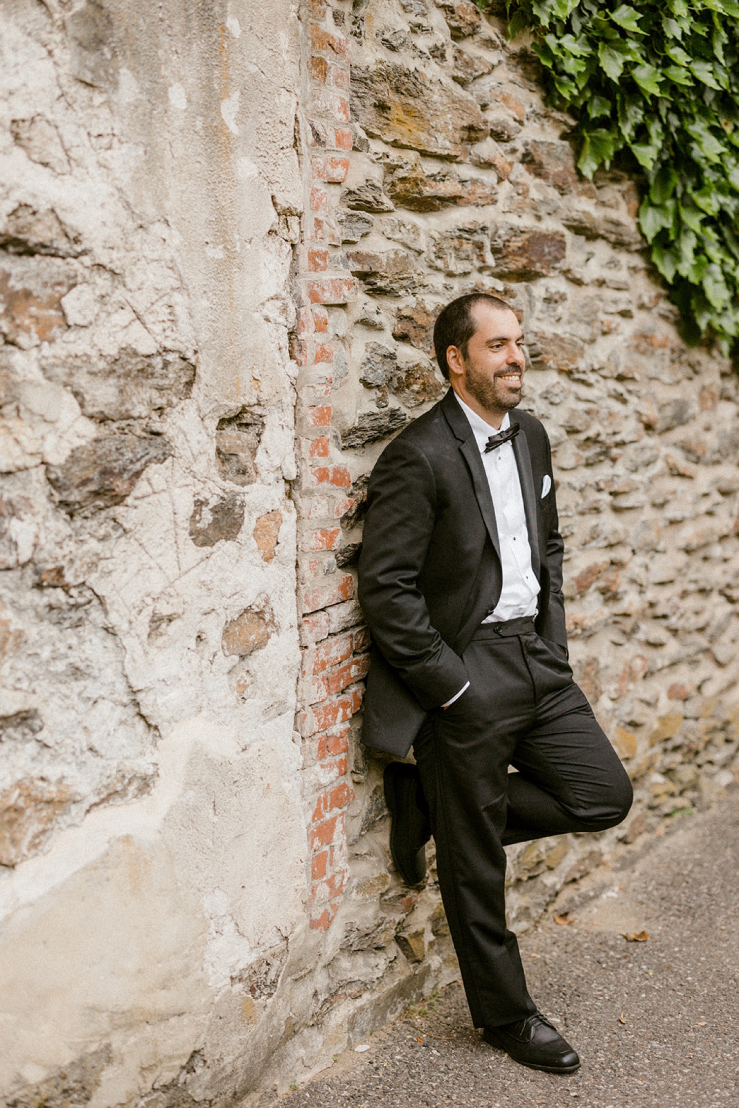 groom leaning against stone wall