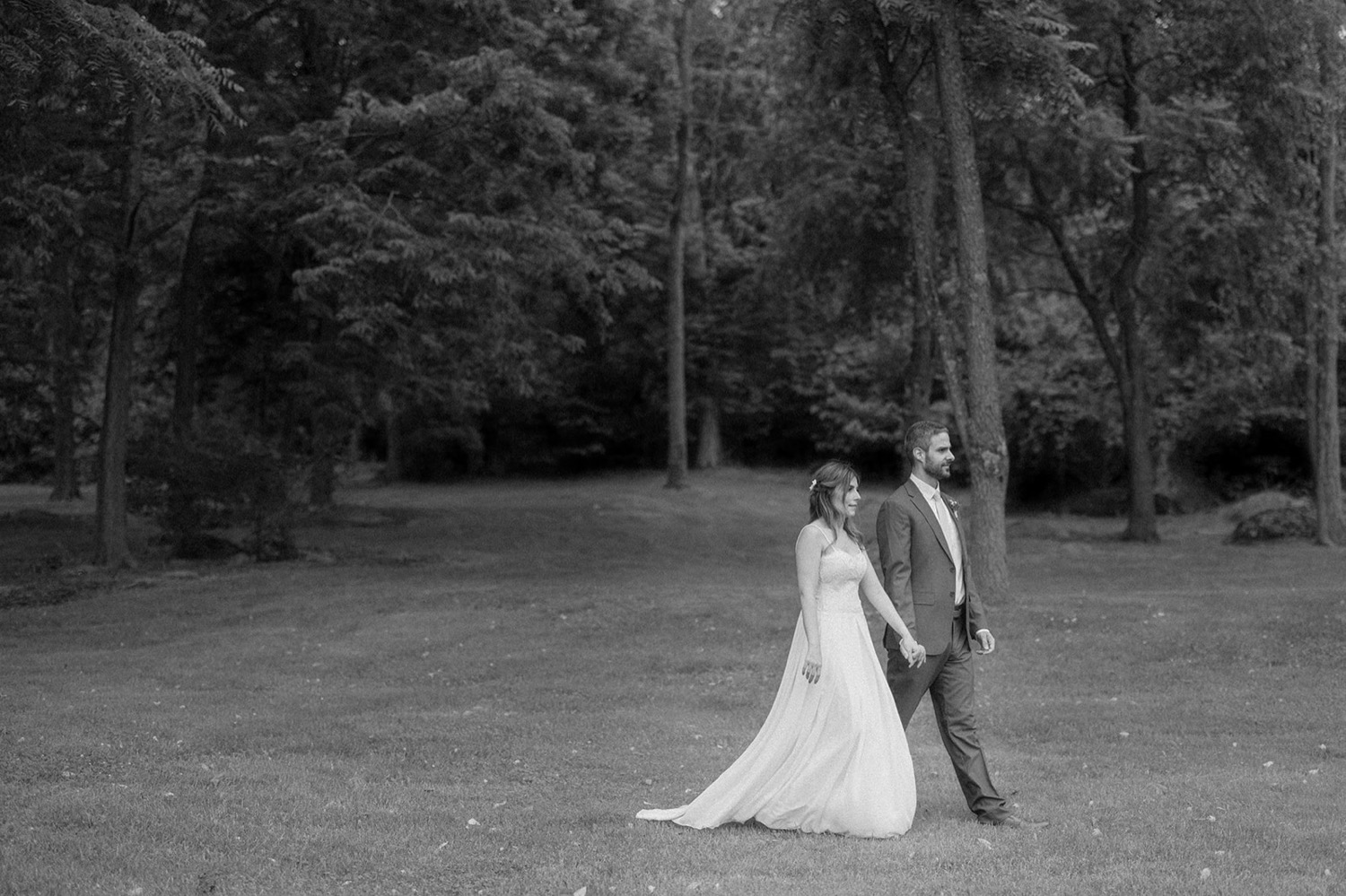 black and white photo of couple walking in wedding outfits holding hands