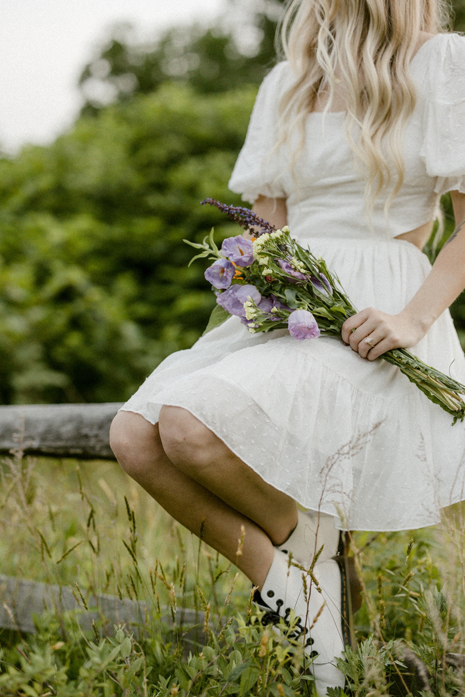 girl in white dress sitting on fence in field with flower bouquet andorra meadows