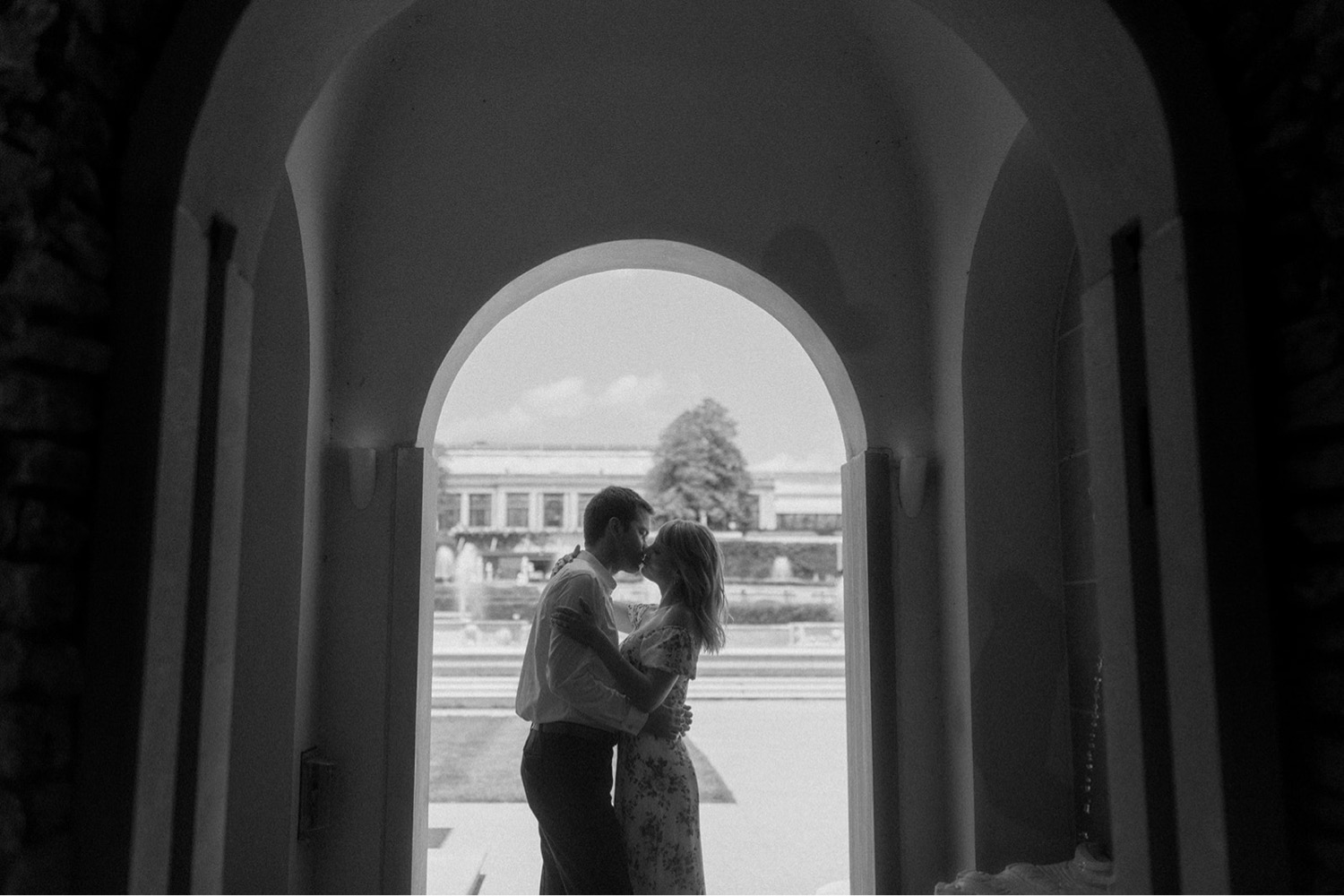 black and white kissing under door arch with fountain in background engagement session