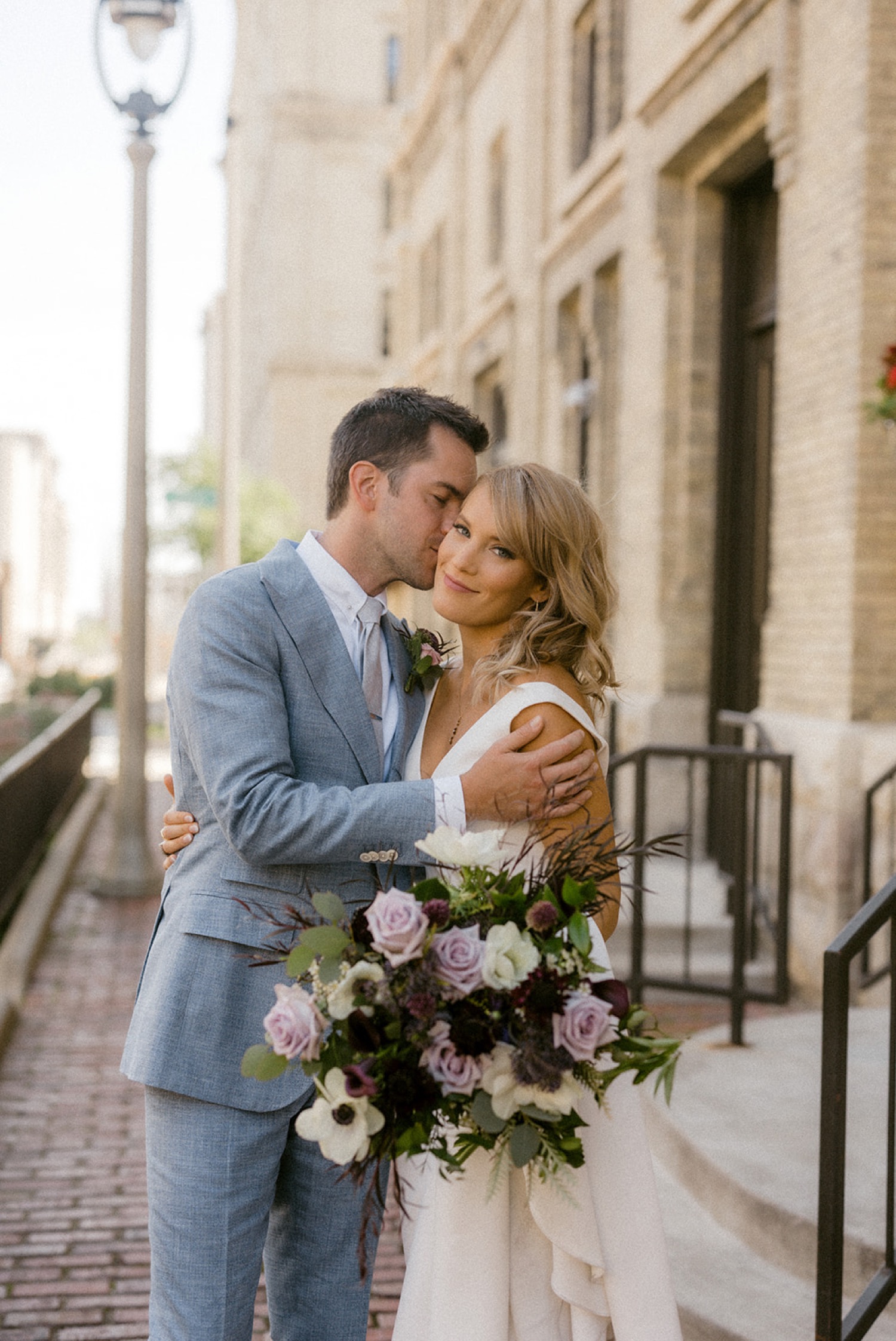 groom kissing brides cheek purple bridal bouquet
