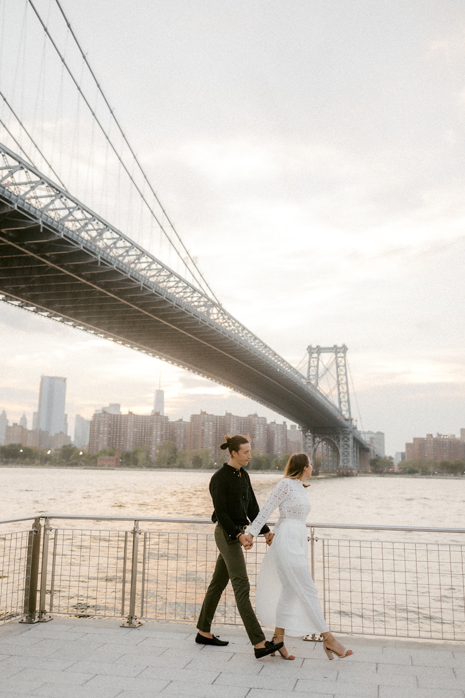 couple walking holding hands under brooklyn bridge