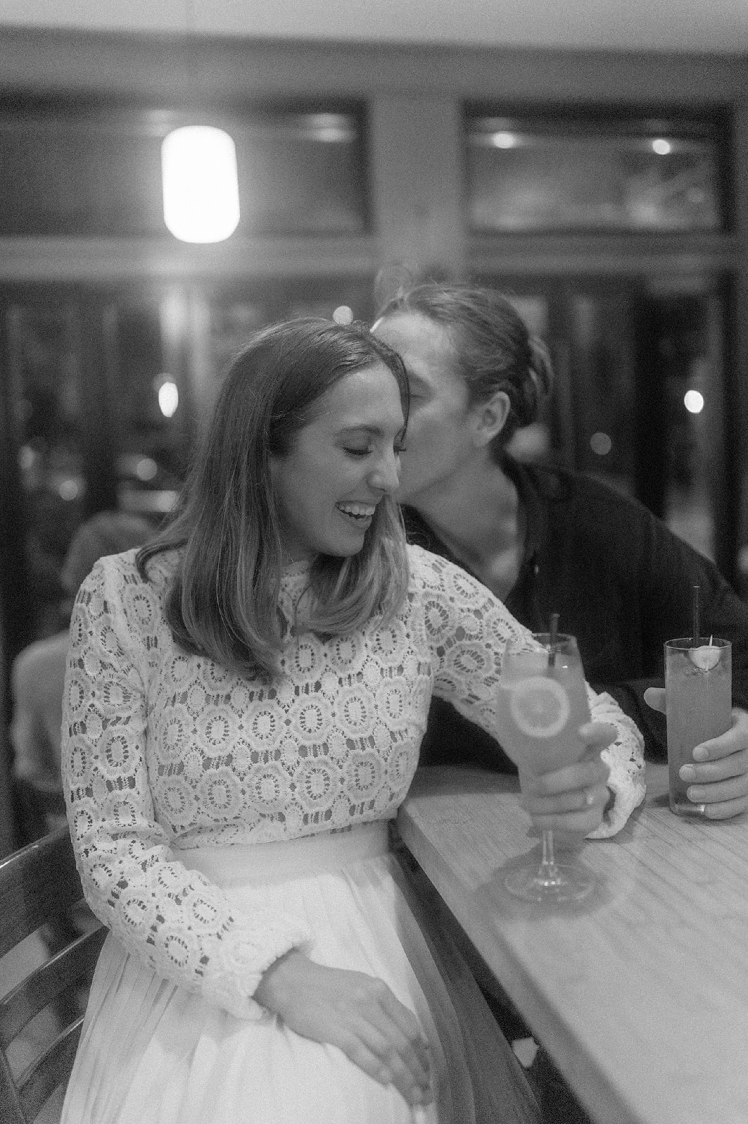 couple drinking cocktails at bar kissing laughing